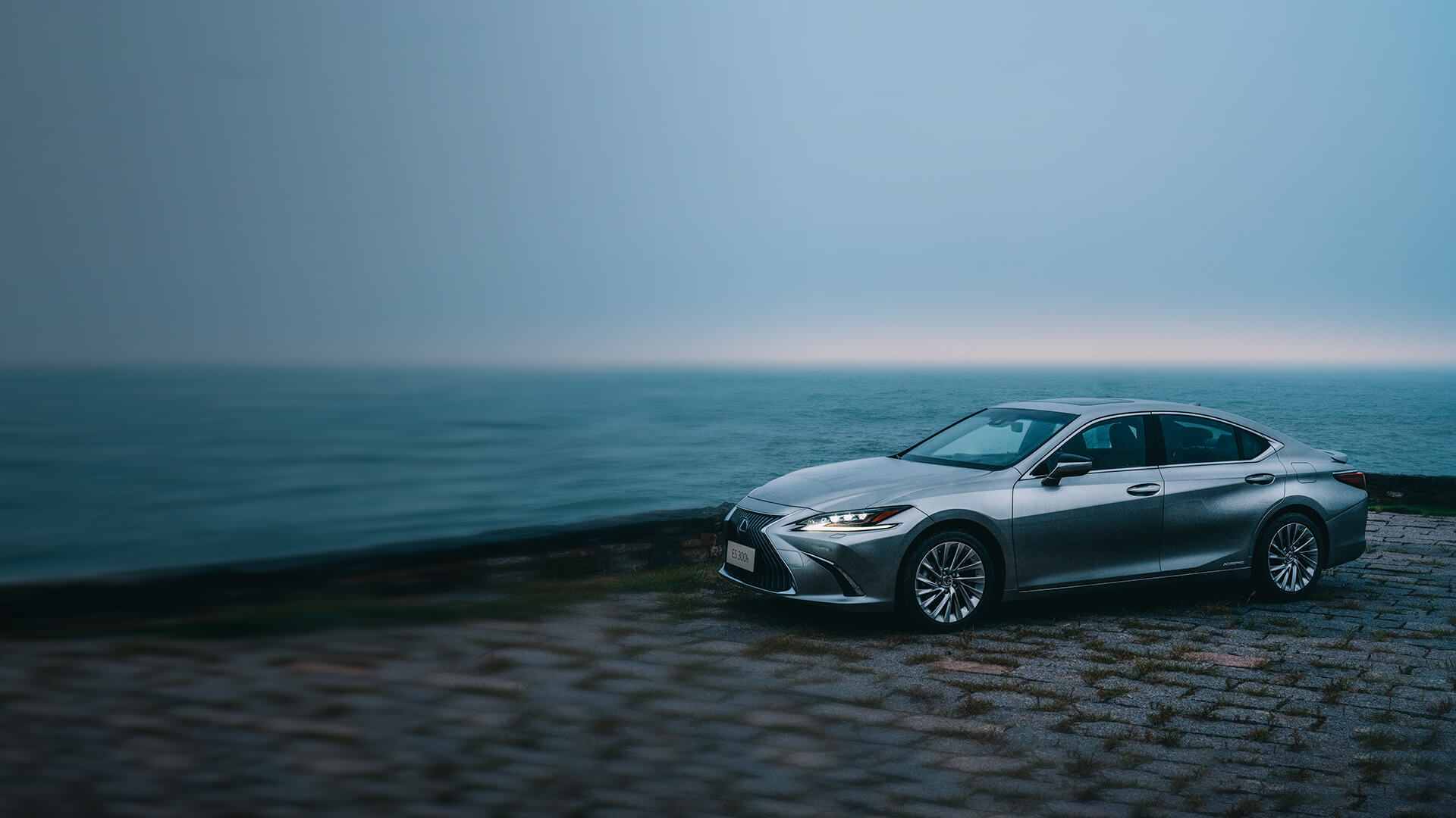 Silver Lexus ES parked on stony ground.