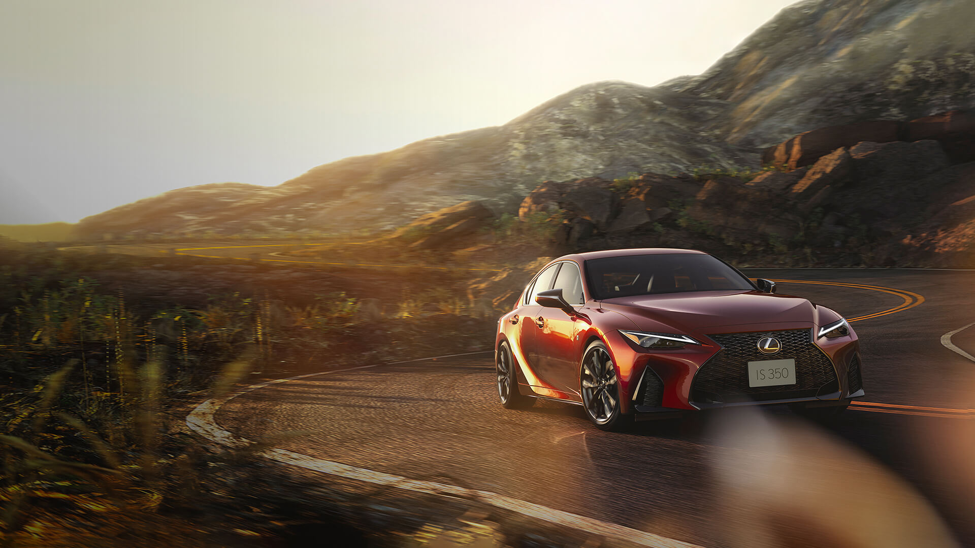 Red Lexus IS being driven on a winding road surrounded by mountainous terrain.